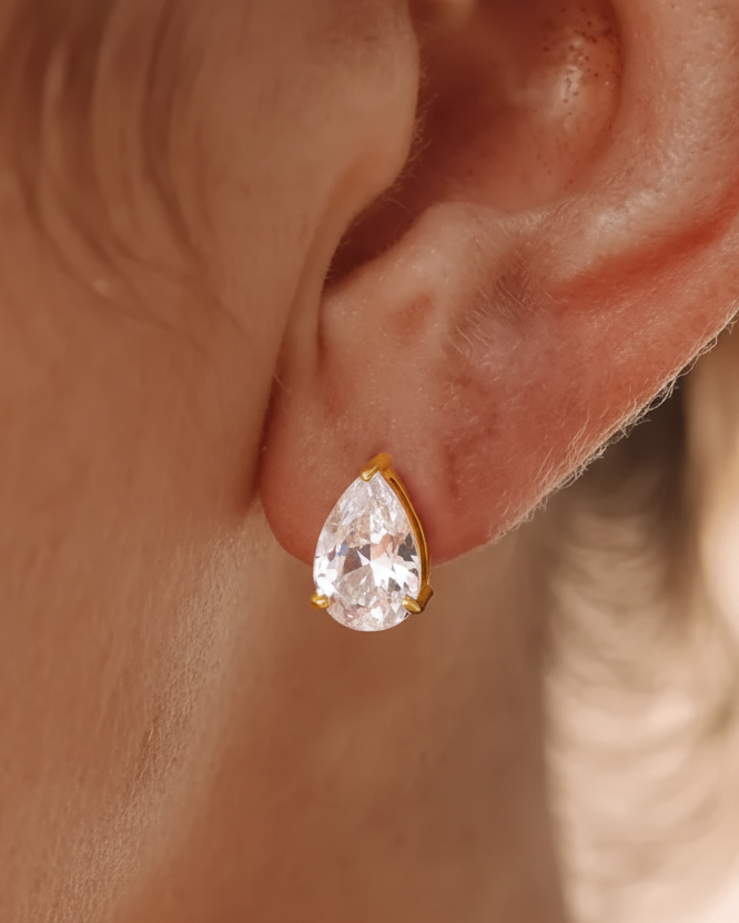 Teardrop-shaped earring worn on an ear with a blurred background
