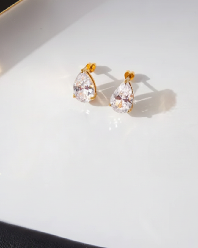 Pair of gold earrings with clear gemstones on a white surface.