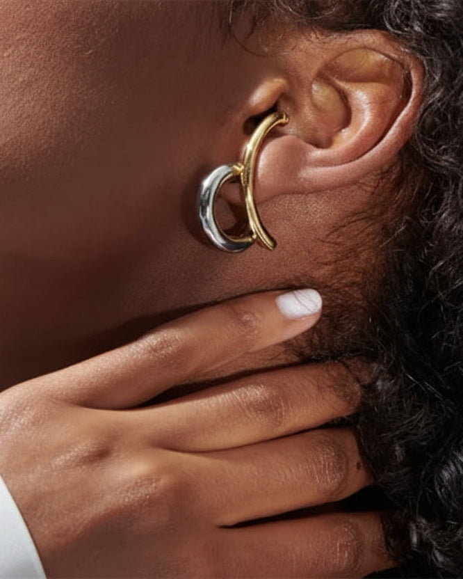Close-up of an ear with a gold and silver hoop earring, hand touching face.