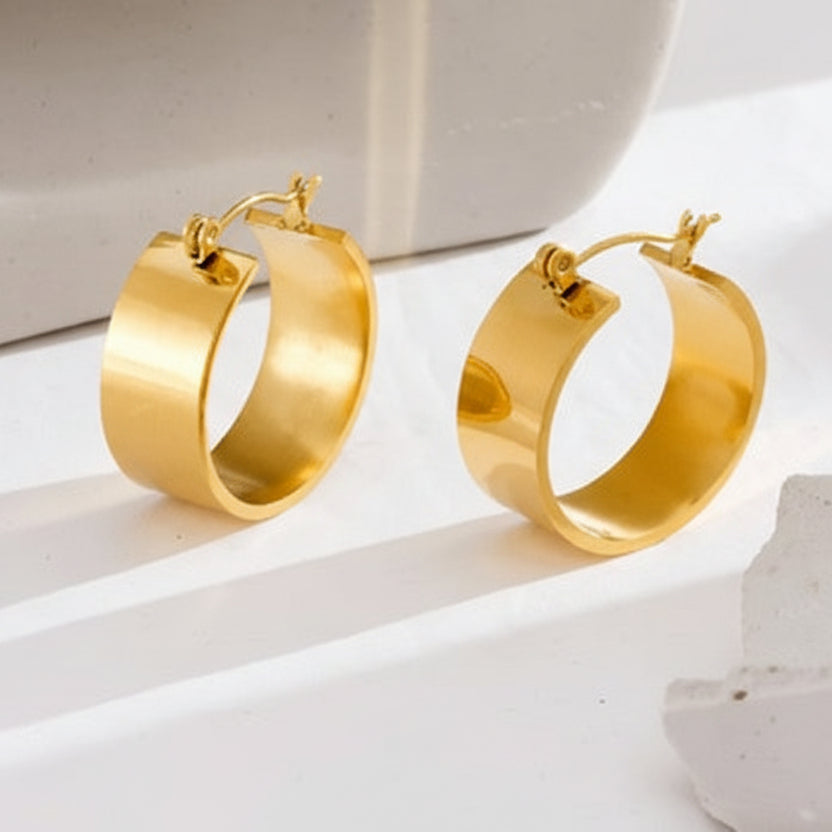 Gold hoop earrings on a white surface with a neutral background