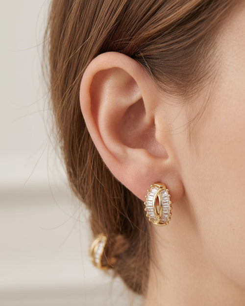Close-up of a person wearing gold hoop earrings with a neutral background