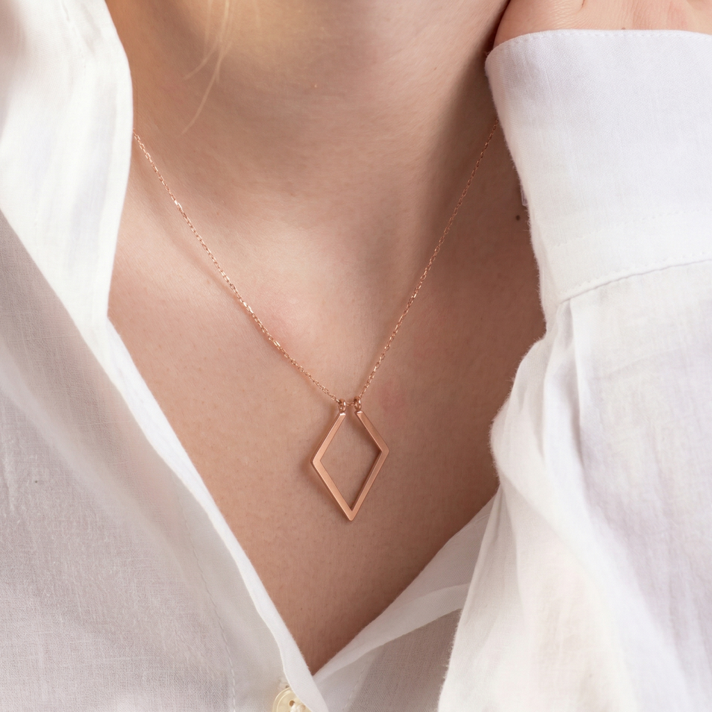 Rose gold necklace with a diamond-shaped pendant worn by a person in a white shirt.