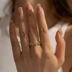 Gold ring with small stones on a person's finger against a neutral background