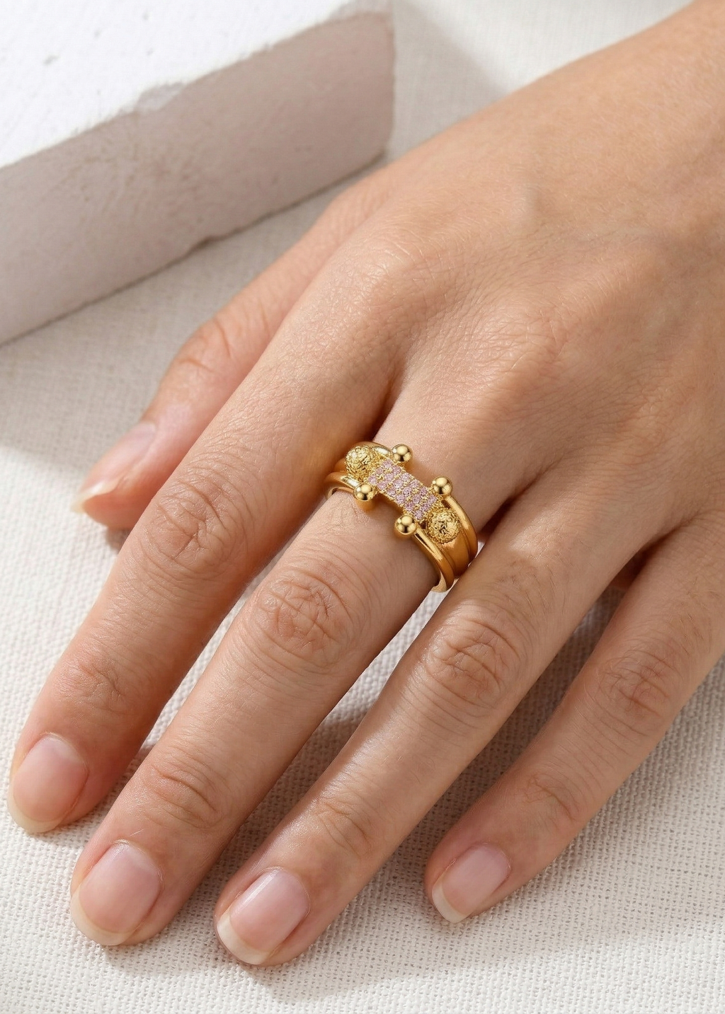 Gold ring with gemstones on a hand against a neutral background