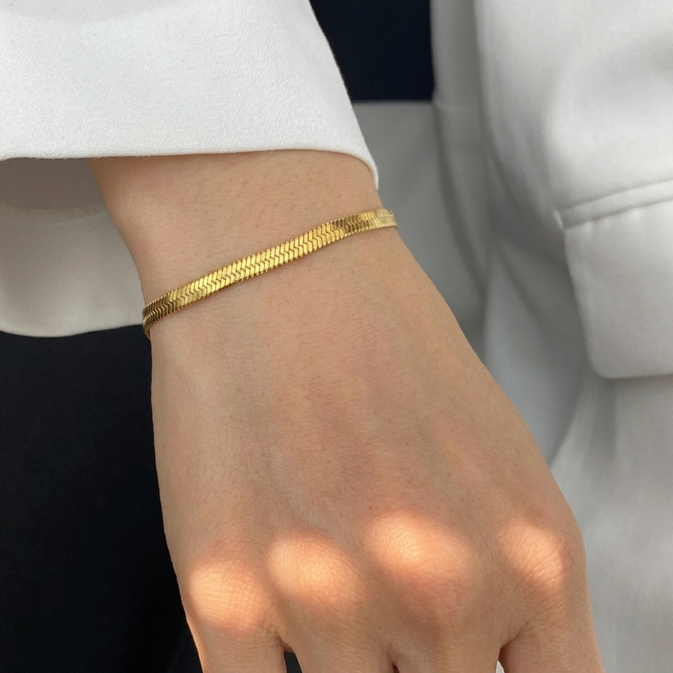 Gold bracelet on a wrist with a neutral background