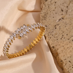 Close-up of a hand wearing a gold bracelet with clear stones on a neutral background