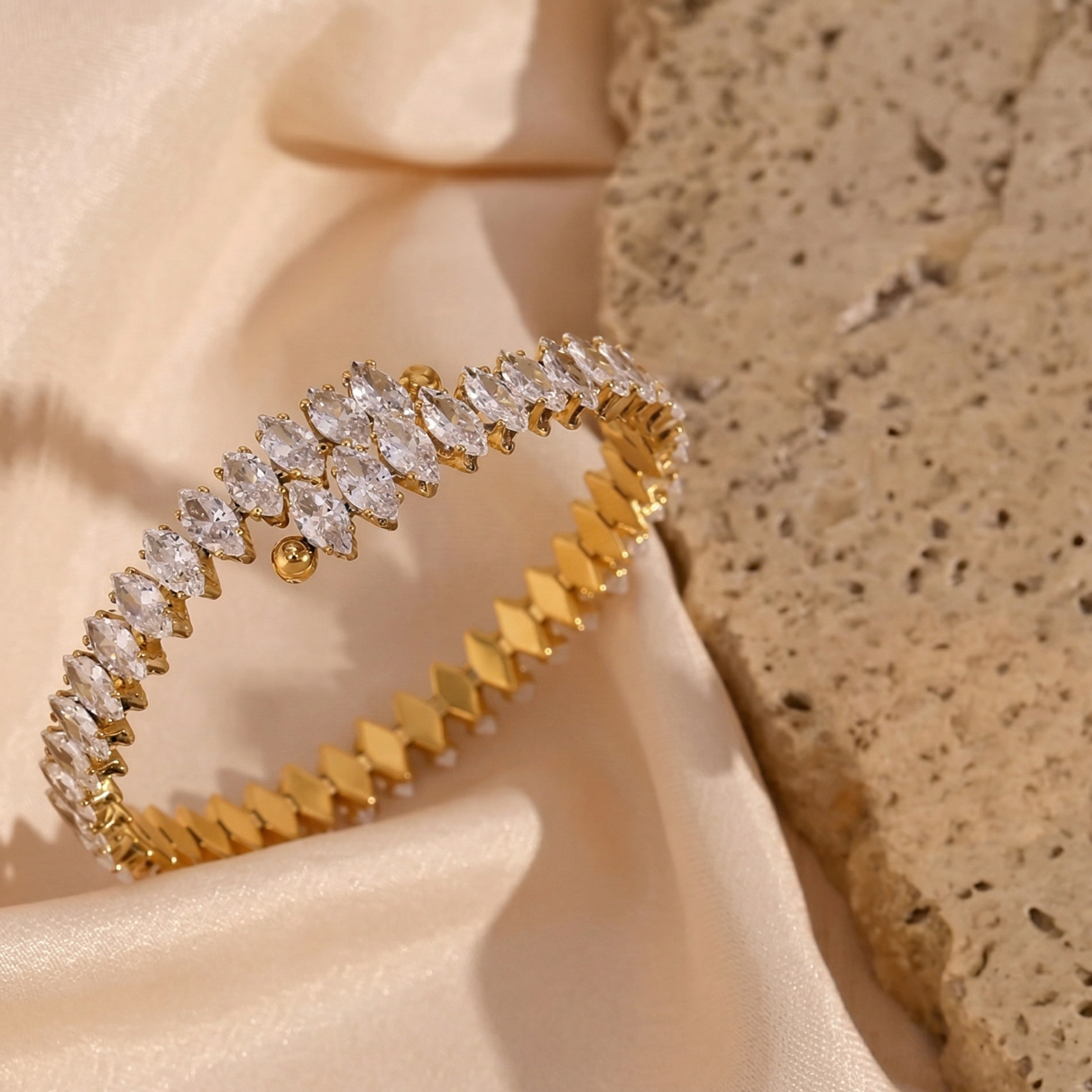 Close-up of a hand wearing a gold bracelet with clear stones on a neutral background