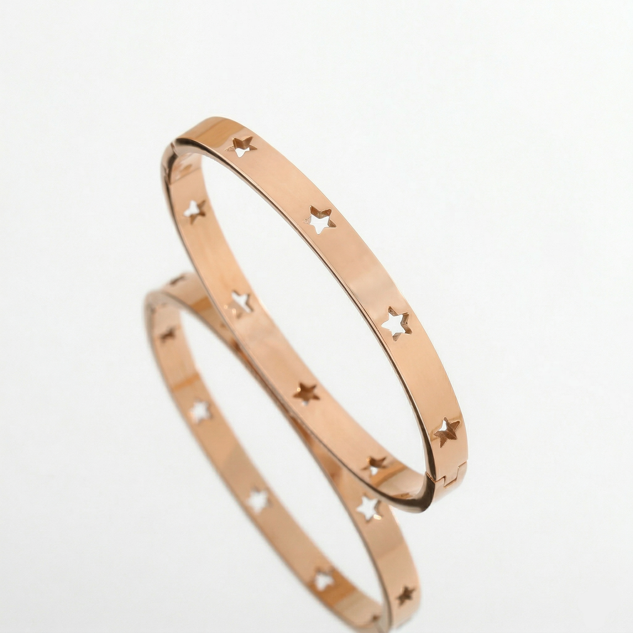 Rose gold bangles with star cutouts on a white background