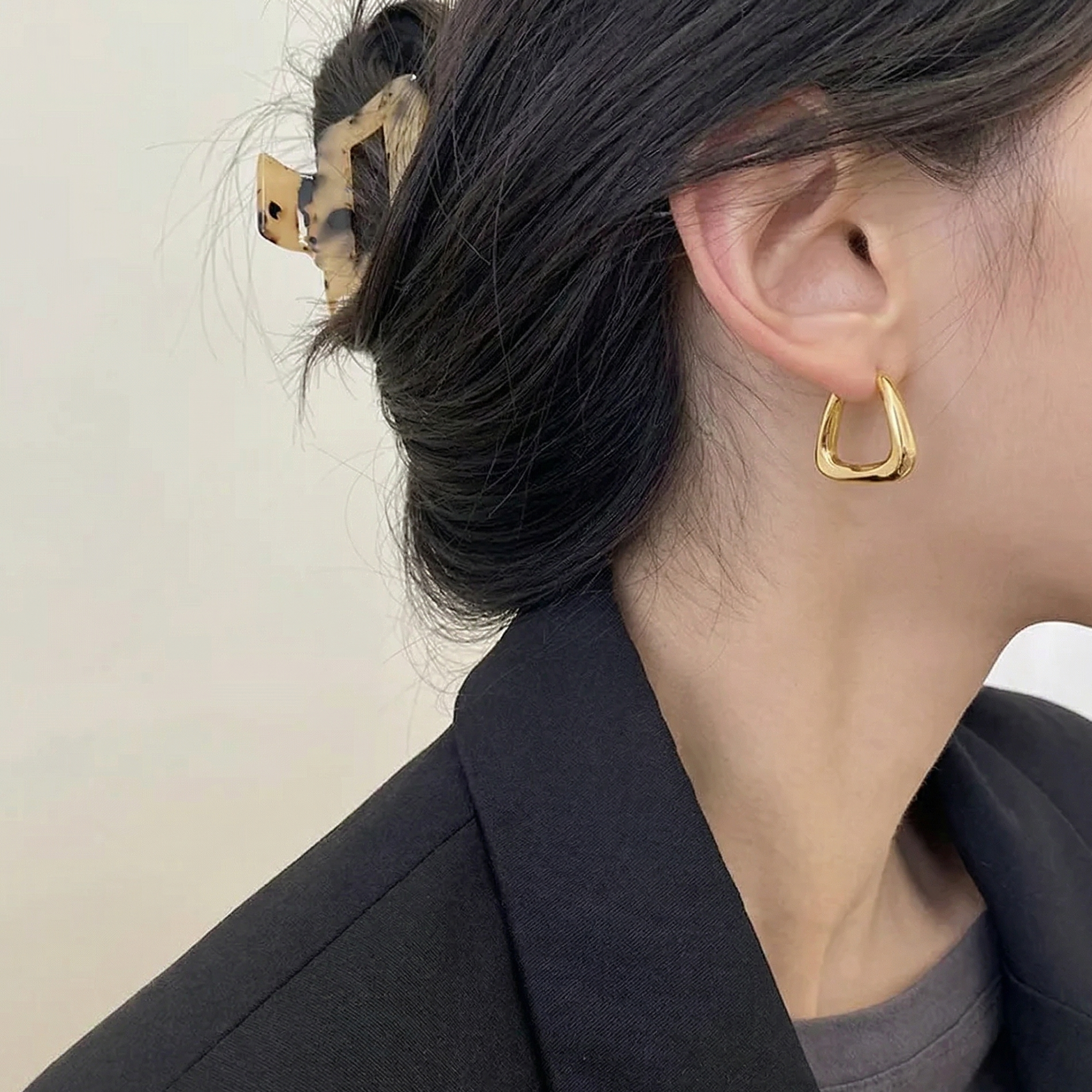 Close-up of a person wearing a gold hoop earring with a neutral background